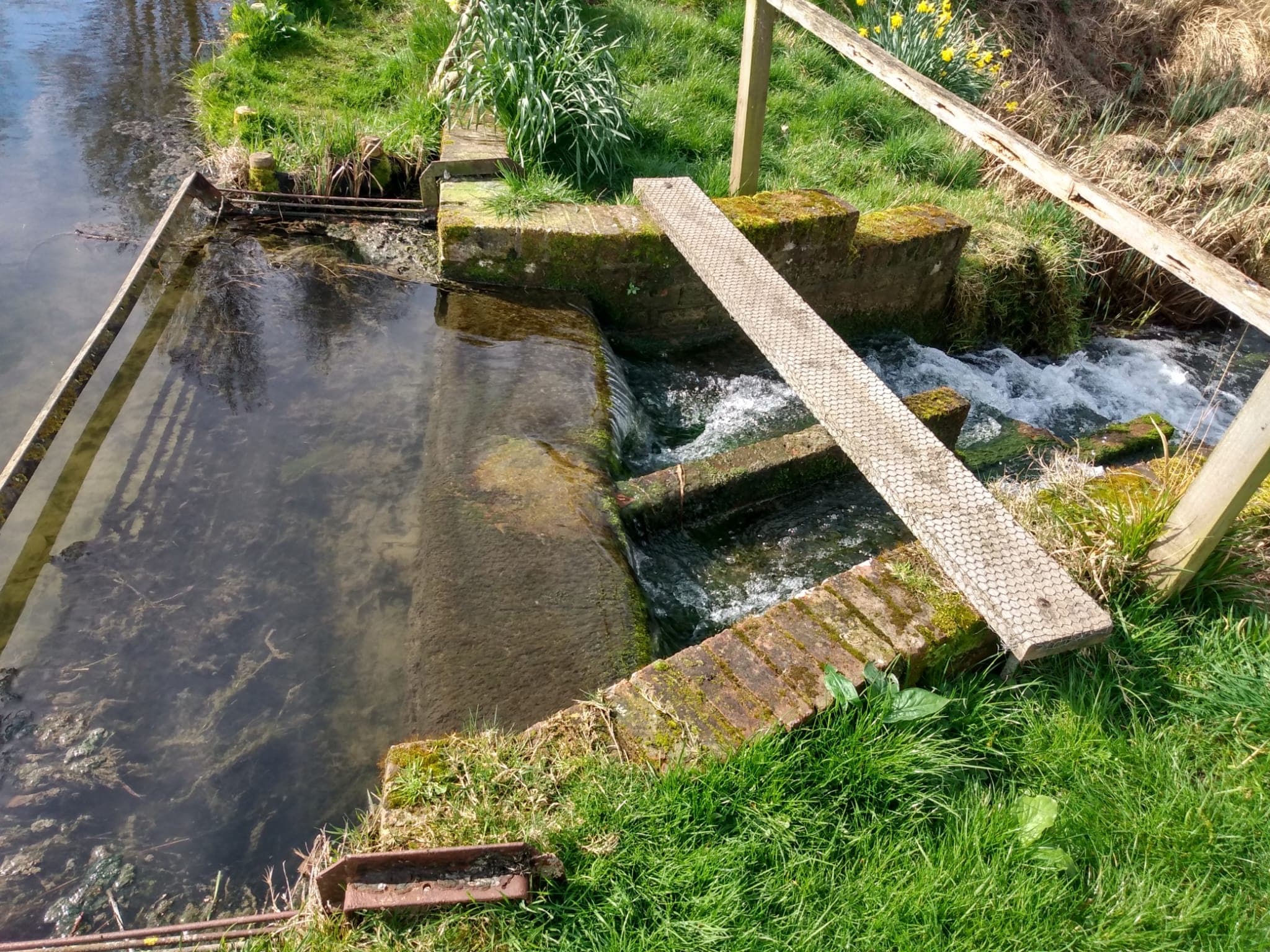 Clear water flowing over the lake outlet weir beside a narrow metal footplate